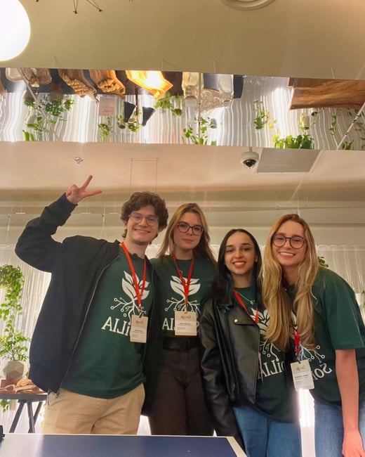 A group of four young adults posing for a photo indoors, wearing matching dark green t-shirts with a logo and Google name tags.