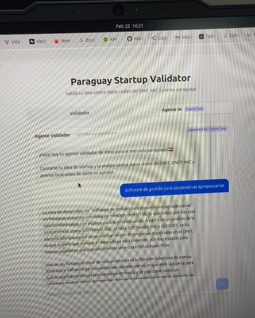 A photograph of a laptop screen displaying a web application named 'Paraguay Startup Validator', which uses AI to analyze startup ideas for the Paraguayan market.