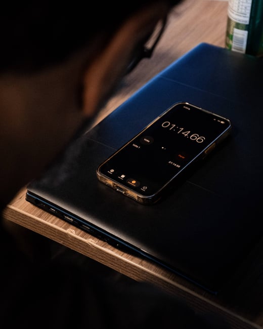 A close-up photograph of a smartphone displaying a running stopwatch timer, resting on top of a closed black laptop.