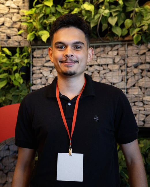 A portrait of a young man with a goatee wearing a black polo shirt and an orange lanyard with a blank white ID badge.