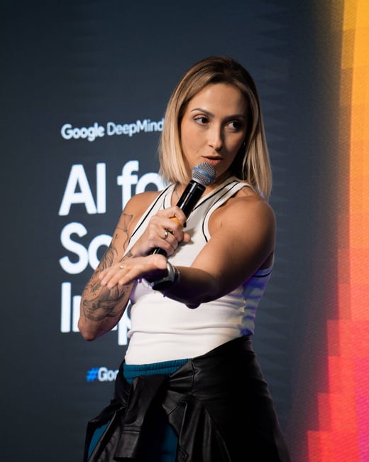 A woman with a tattoo on her arm is speaking into a microphone during a presentation at a Google DeepMind event.