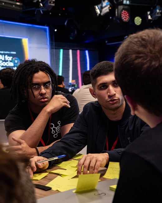 Two young men are deeply engaged in a collaborative discussion at a table covered with yellow sticky notes during a tech event.
