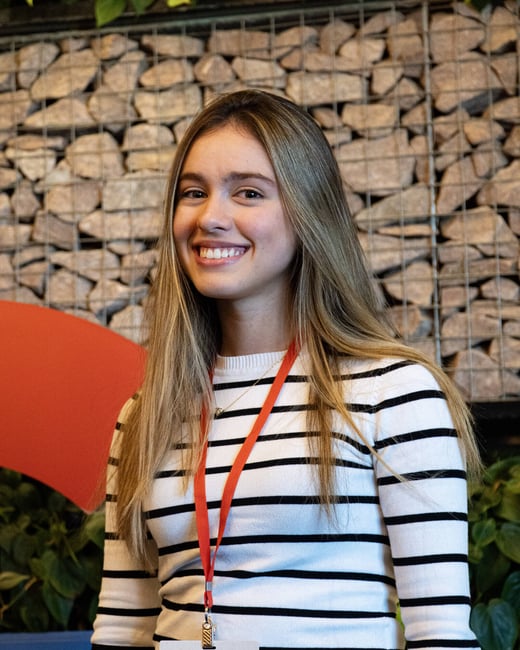 A portrait of a smiling young woman with long blonde hair wearing a black and white striped sweater and a Google lanyard.