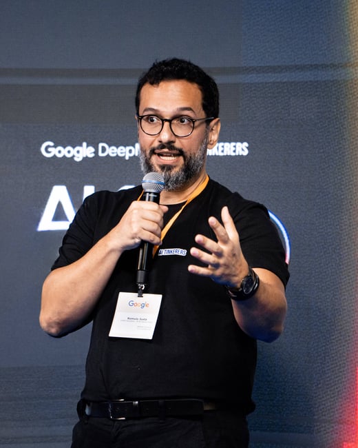 A man with glasses and a beard is speaking into a microphone and gesturing with his hand during a presentation.