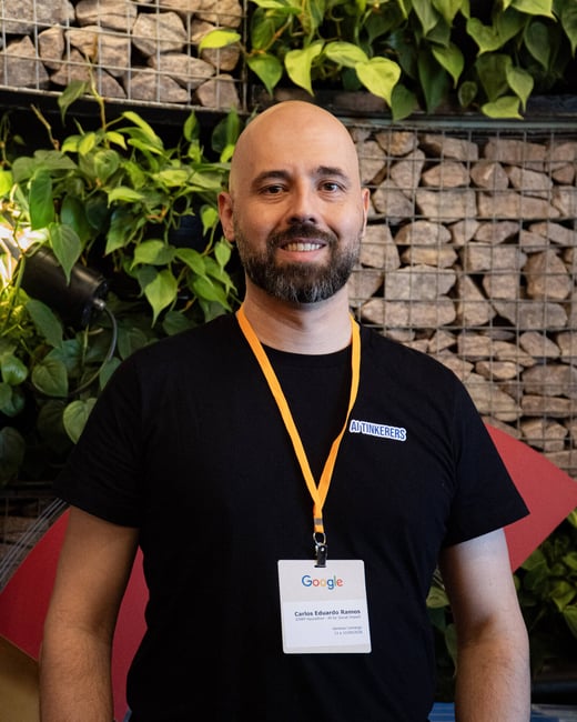 A portrait of a man named Carlos Eduardo Ramos smiling while wearing an AI Tinkerers t-shirt and a Google event badge.