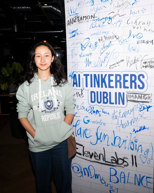 A young woman in a light green Ireland Republic hoodie stands next to a white signature board filled with handwritten names and the text 'AI TINKERERS DUBLIN'.