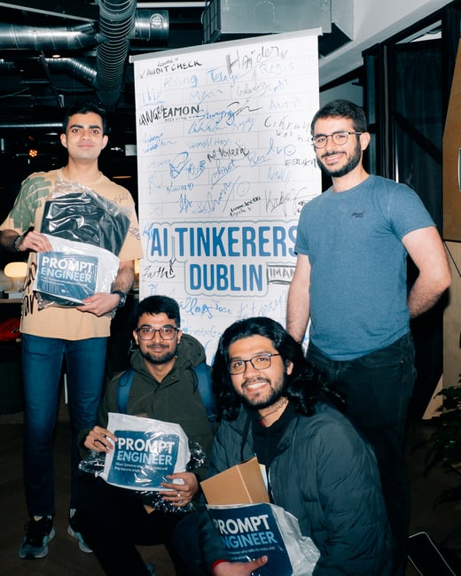 Four men pose together indoors in front of an 'AI Tinkerers Dublin' banner covered in signatures, with three of them holding 'Prompt Engineer' swag bags.