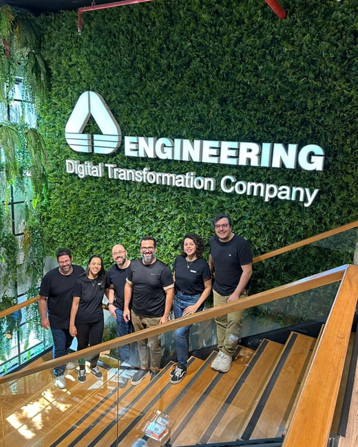 A group of six people posing for a photo on a wooden staircase in front of a lush green plant wall featuring a company logo.