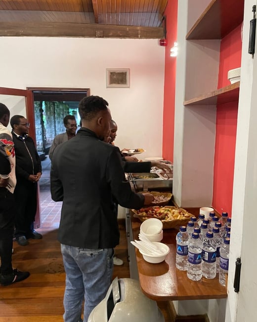 A group of people are lined up at an indoor buffet station, serving themselves food and picking up bottled water.