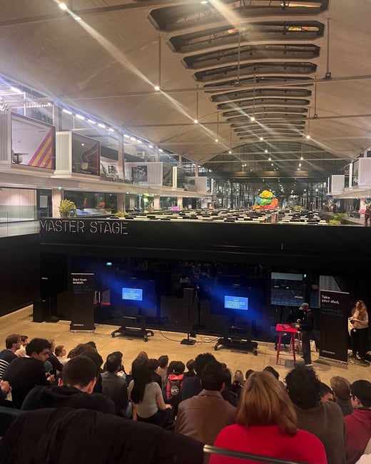 A photograph captures a presentation taking place on the 'MASTER STAGE' in a large, indoor event venue with a high, architecturally distinctive ceiling, viewed from the back of a seated audience.