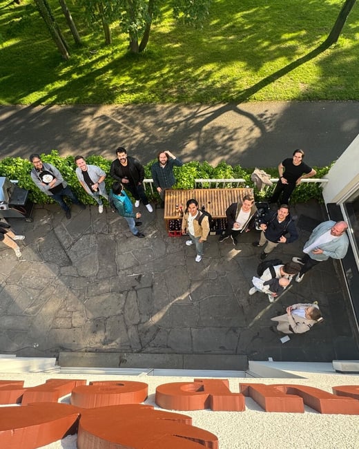 A high-angle photograph looking down at a group of people gathered on a stone patio outside a building, with many looking up towards the camera.