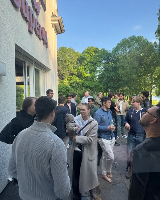 A group of people are gathered outdoors for a social event next to a building with a 'Super44' sign.