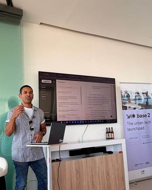 A man stands next to a standing desk and laptop, delivering a presentation in front of a large screen showing a software interface.