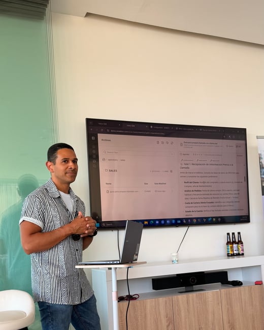 A man stands next to a large display screen showing a document in Spanish, with a laptop on a small white stand in front of him.