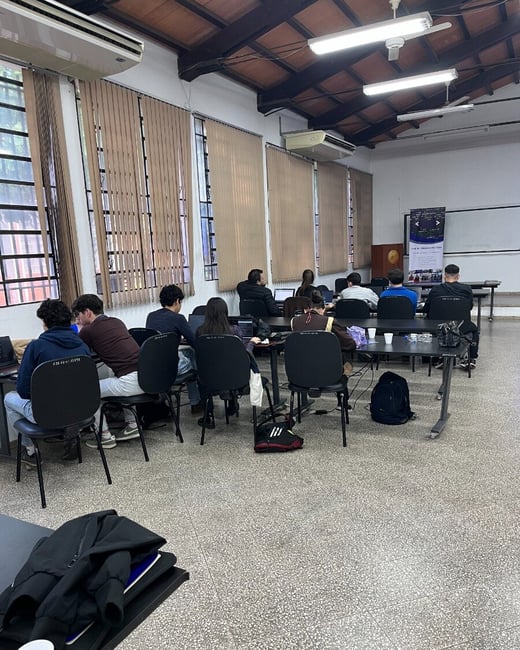 A group of students are sitting at desks with their laptops open in a classroom, likely attending a programming club session.