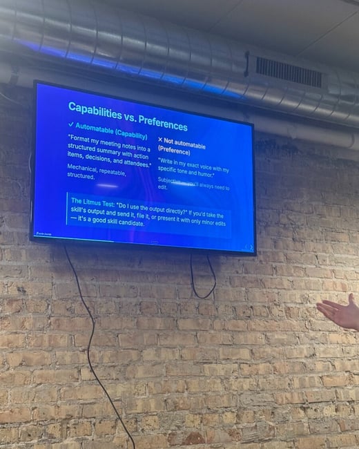A photograph of a television screen mounted on a brick wall, displaying a presentation slide about the differences between automatable capabilities and non-automatable preferences.