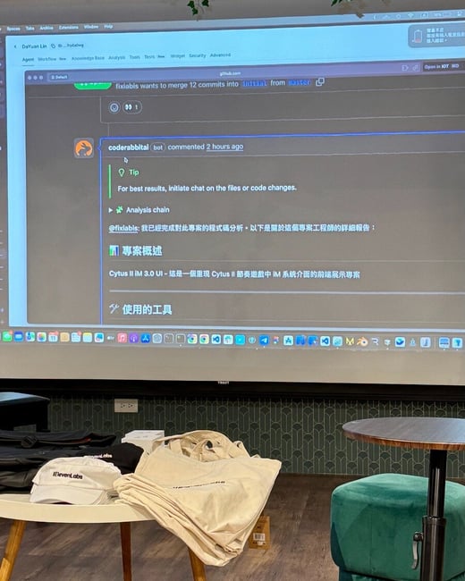 A photograph taken indoors showing a large screen displaying a GitHub interface with a bot's code analysis report written in both English and Traditional Chinese, with promotional merchandise (caps and tote bags labeled 'ELEVENLABS') resting on a small white table in the foreground.