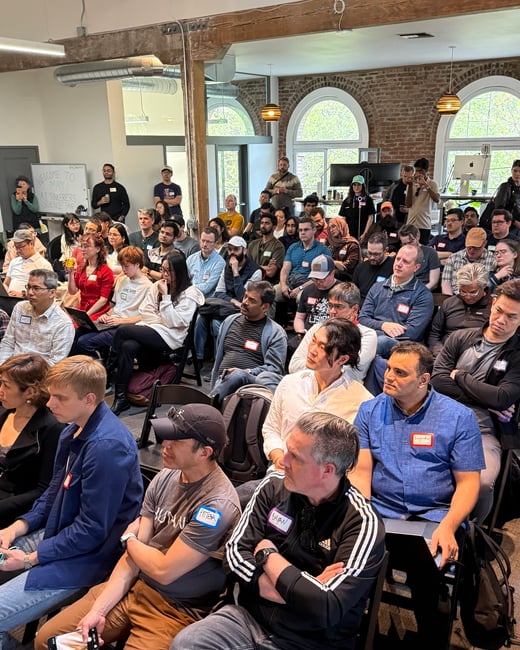 A large group of people are seated in an indoor event space, attending the May AI Tinkerers Science Fair.