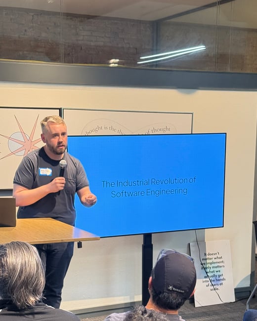 A man stands in front of a large blue screen giving a presentation titled 'The Industrial Revolution of Software Engineering' to a seated audience.