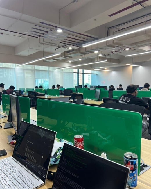 A wide-angle photograph of a modern open-plan office where several people are working at desks separated by vibrant green privacy screens.
