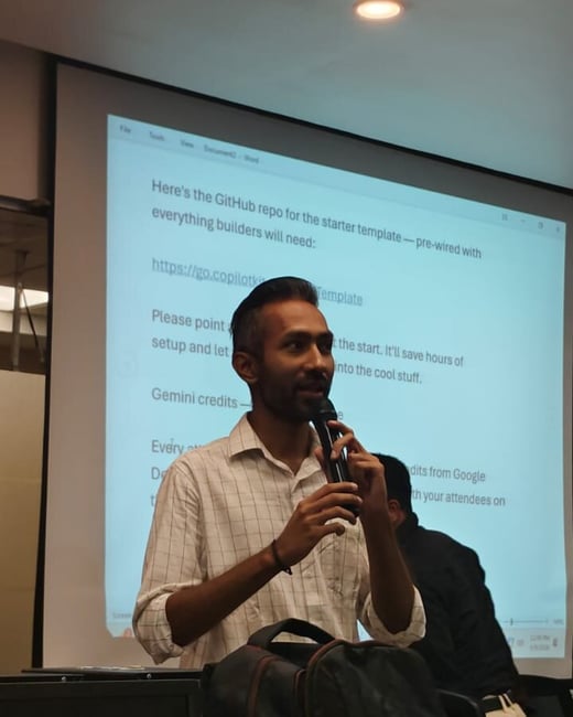 A man is giving a presentation while holding a microphone in front of a projector screen displaying text about a GitHub repository.