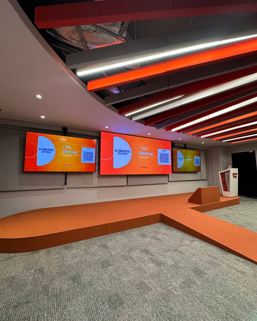 An empty modern presentation stage set up for an 'AI Tinkerers São Paulo' meetup, featuring large screens and an orange platform.