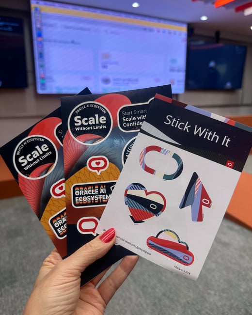 A close-up photograph of a hand with red nail polish holding three Oracle AI Ecosystem promotional stickers in a conference-like setting with a blurred screen in the background.