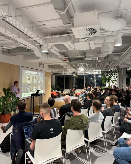 A speaker stands at the front of a room giving a presentation to a seated audience at a tech event called 'AI Tinkerers Warsaw'.