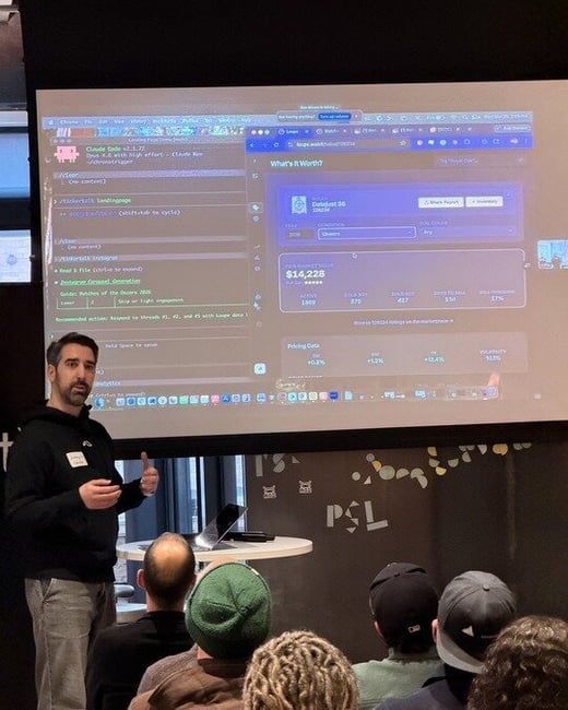 A man stands in front of a projection screen giving a technical presentation to an audience. The screen displays a coding interface and a watch market valuation dashboard.