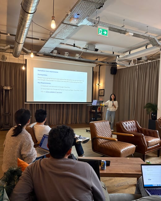 A woman is giving a presentation about Hackathon requirements to a small group of people in a modern indoor space with leather armchairs.