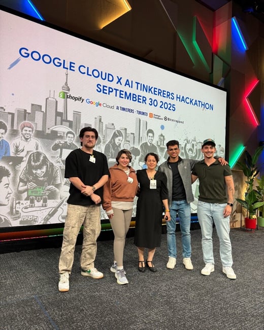 A group of five individuals stands posing on a stage in front of a large projection screen that advertises the 'GOOGLE CLOUD X AI TINKERERS HACKATHON' event.