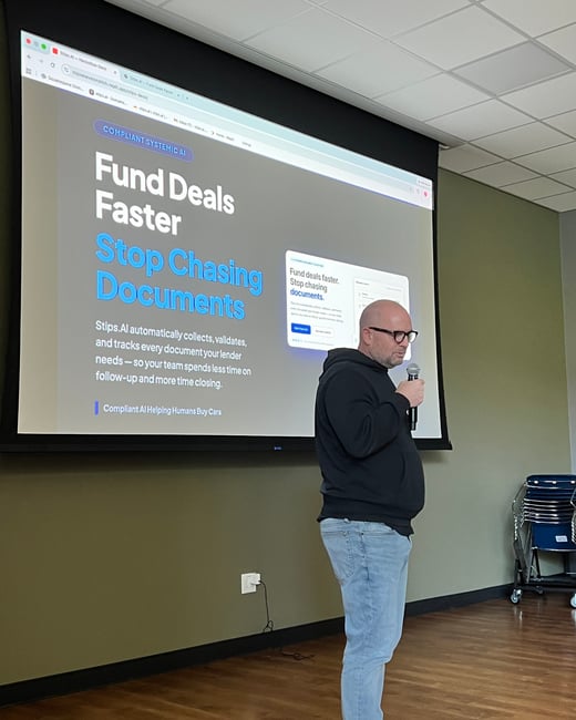 A man in a black hoodie and glasses stands in front of a large projection screen, giving a presentation about a software called Stips.AI.