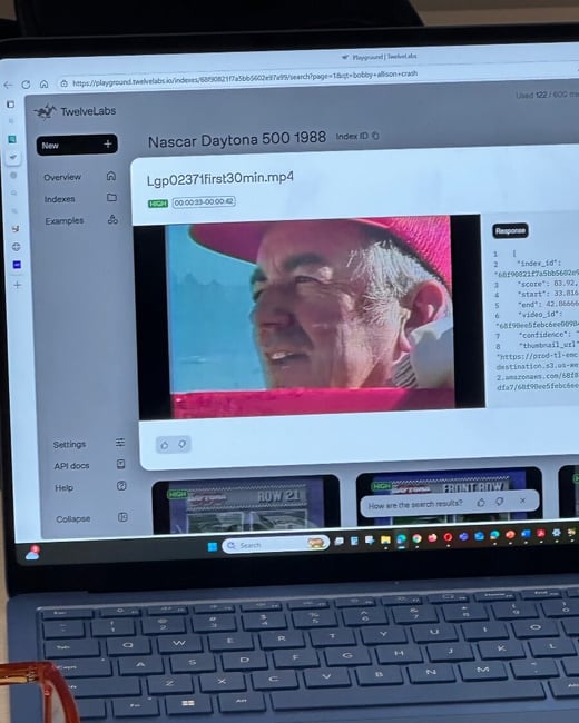 A close-up photograph of a laptop displaying a web application interface for video indexing (TwelveLabs Playground), featuring a video frame of a man wearing a red hat from a Nascar Daytona 500 1988 clip.