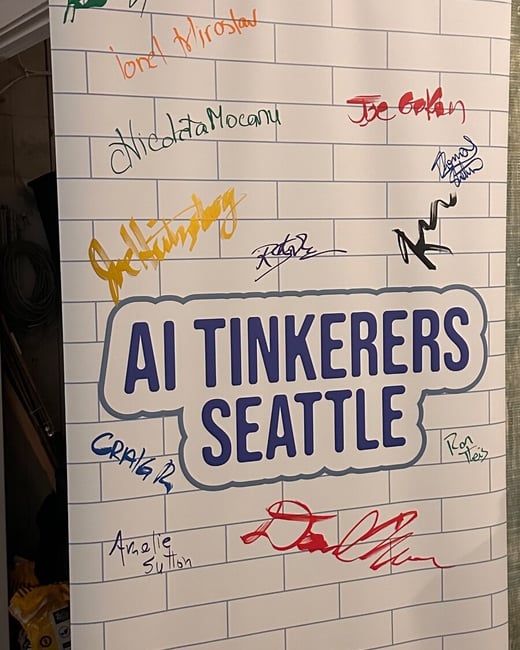A photograph of a pull-up event banner for the “AI TINKERERS SEATTLE” group, featuring a white background with a light gray subway tile pattern and covered extensively with numerous handwritten signatures in various colors.