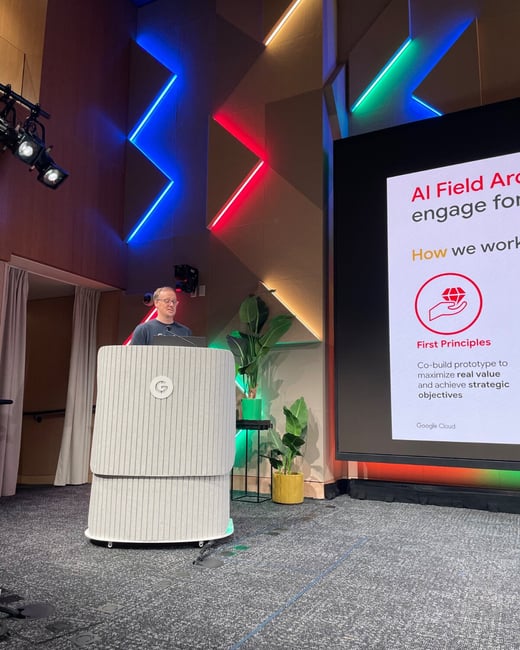 A man stands behind a modern, striped podium delivering a presentation on a stage decorated with colorful zigzag neon lights (blue, red, and green) against a wooden wall.