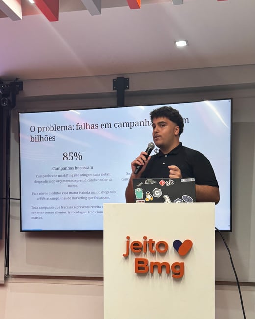 A man is giving a presentation behind a white podium with the 'jeito Bmg' logo, while a screen behind him displays statistics in Portuguese about marketing campaign failures.