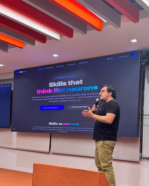A man stands on an orange stage giving a presentation in front of a large screen displaying a website for 'SkillsChain'.
