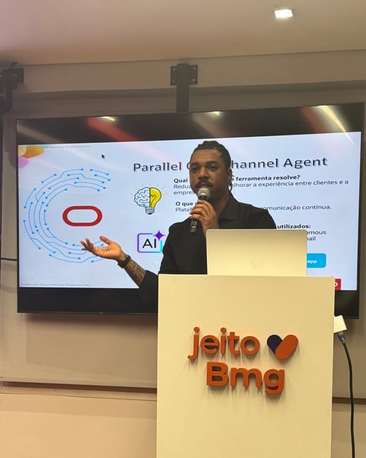 A man stands behind a podium labeled 'jeito Bmg' while giving a presentation with a slide titled 'Parallel Channel Agent' displayed on a large screen behind him.