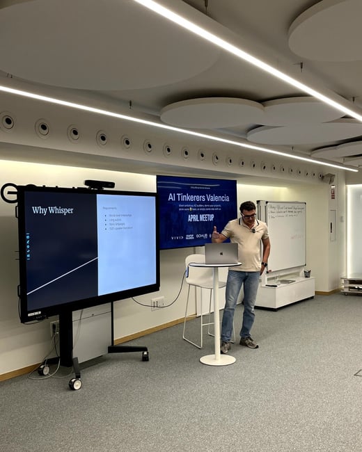 A man stands in a modern event space, delivering a presentation titled 'Why Whisper' during an 'AI Tinkerers Valencia' meetup.