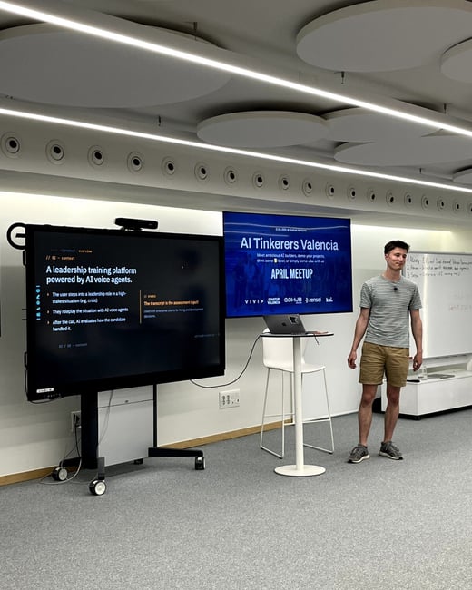 A man stands in a modern presentation room next to two large screens displaying information about an AI meetup and a leadership training platform.