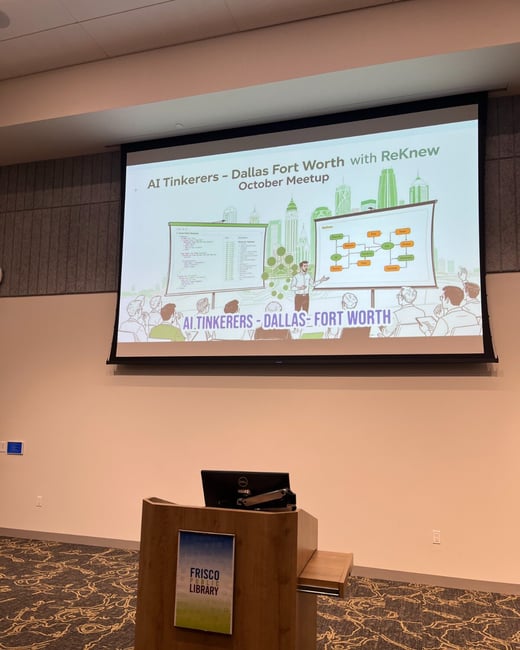 A photograph showing the setup of an indoor presentation room, featuring a large screen displaying the title slide for the 'AI Tinkerers - Dallas Fort Worth October Meetup' and a wooden lectern labeled 'FRISCO PUBLIC LIBRARY.'