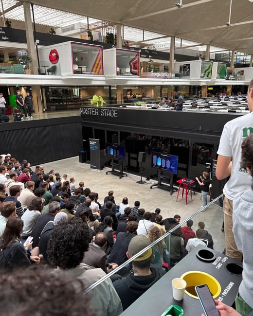 A high-angle photograph captures a large audience seated in a tiered, modern indoor atrium attending a presentation held on the "MASTER STAGE," with screens displaying content and "Google for Startups" branding visible on the upper level.