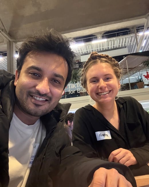 A close-up selfie shows a man and a woman smiling happily at the camera in a low-light setting, likely at a social or networking event, as the woman is wearing a name tag reading 'Kineta'.