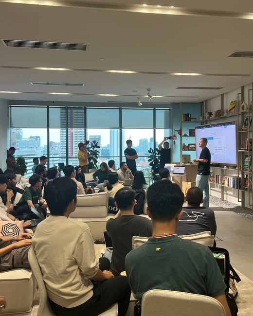 A man gives a presentation to an audience in a modern office space with large windows overlooking a city skyline.