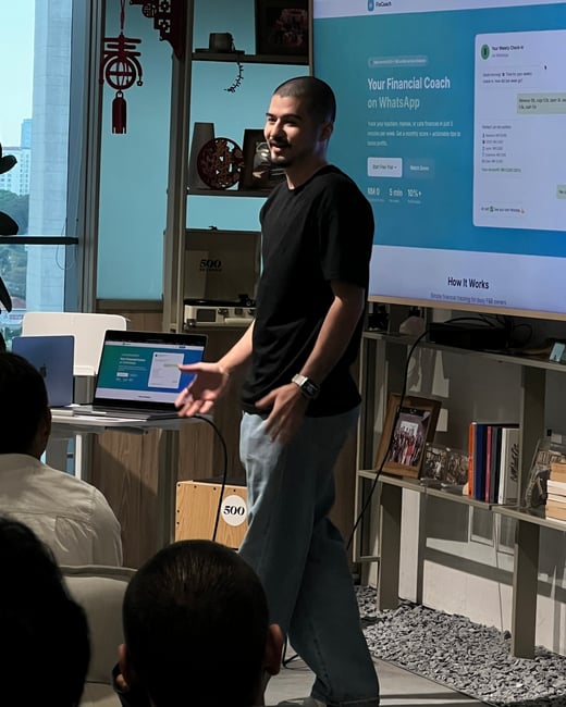 A man stands in front of a large screen giving a presentation about a financial coaching service called FinCoach to an audience.