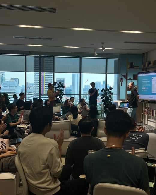A group of people are gathered in a modern office space with large windows overlooking a city skyline, attending a presentation.