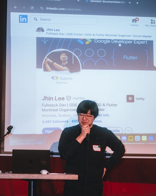 A photograph showing a man named Jhin Lee speaking into a microphone during a presentation, with his LinkedIn profile projected on a large screen behind him.