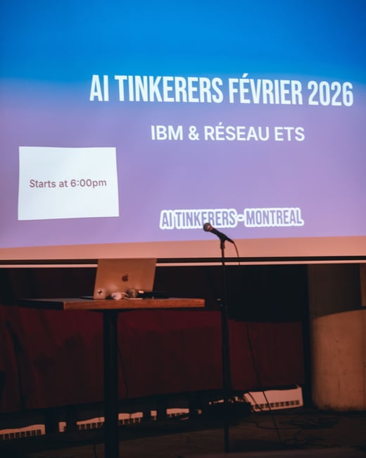 A photograph of a projection screen at an event venue displaying information for an 'AI Tinkerers' meetup in Montreal. Below the screen, a laptop sits on a small podium next to a microphone stand.