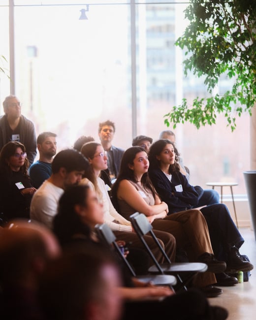 An audience of people sitting in a bright, modern indoor space, attentively watching a presentation or event.