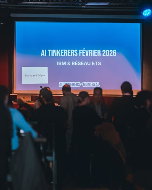 A photograph of an indoor event where an audience is gathered in front of a large projection screen displaying information about an 'AI Tinkerers' meetup in Montreal.